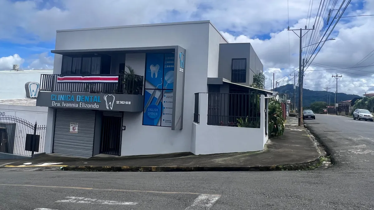 Fachada de la clínica: edificio esquinero blanco de dos plantas con el rótulo Clínica Dental Dra. Ivannia Elizondo